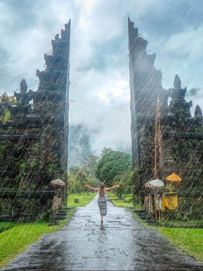 Woman in vibrant rain at iconic Handara Gate, Bali. A magical travel moment.